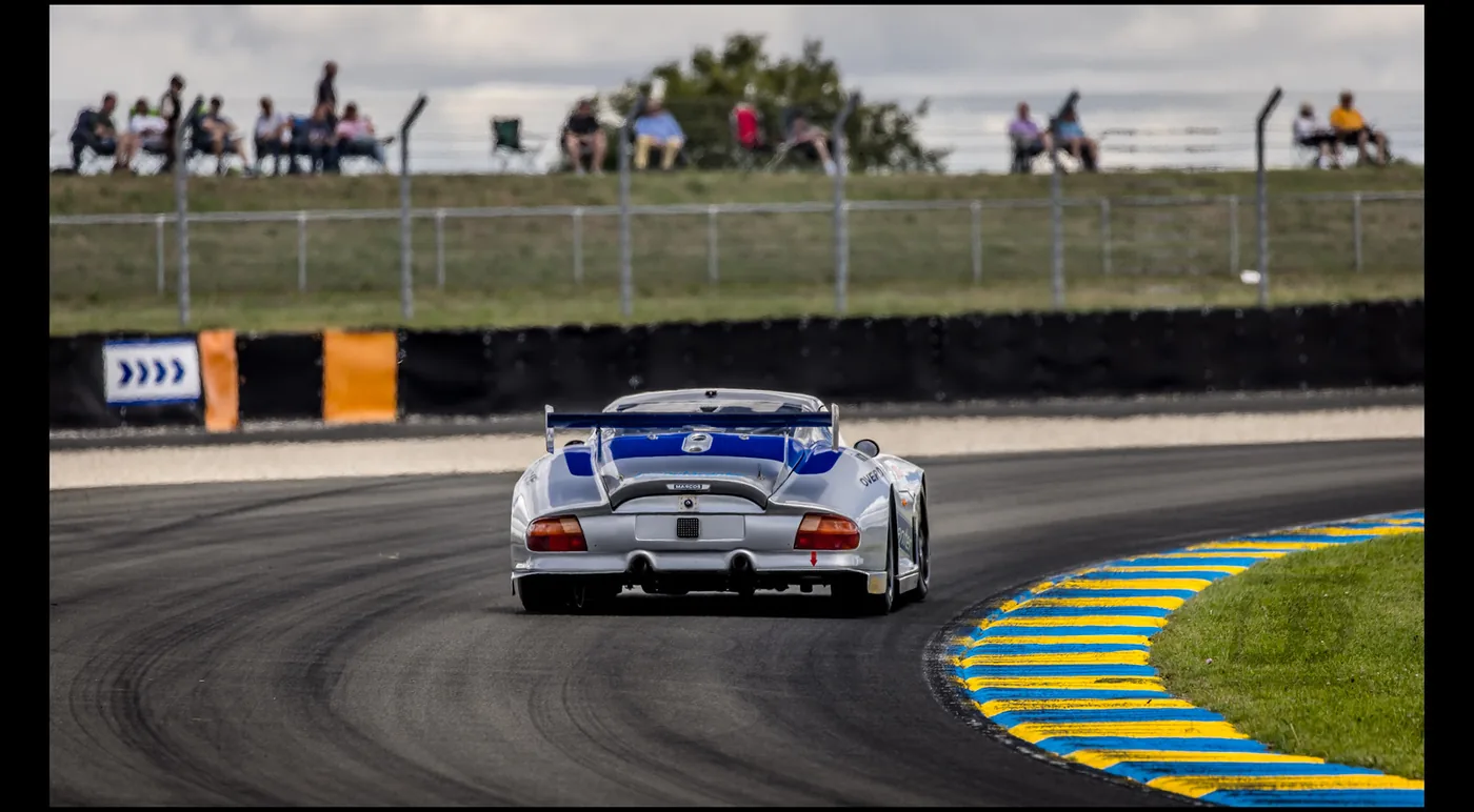 A silver and blue Marcos LM600 racing car photographed rear-on, mid-corner on a circuit